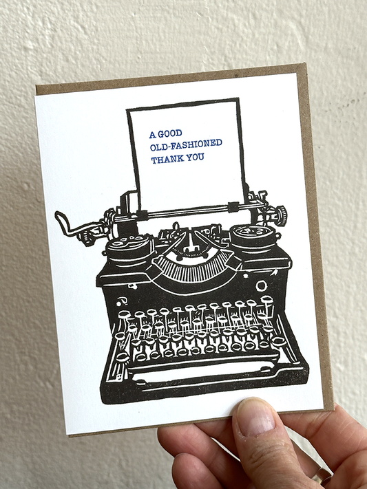 Thank you letterpress card front held in hand, showing black typewriter print and text.