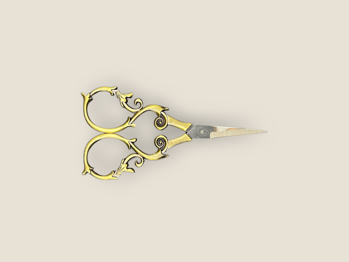 Ornate gold-toned scissors laid sideways with curled filigree handles