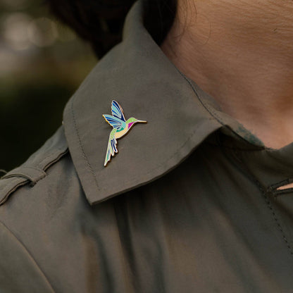 Hummingbird enamel pin attached to a dark jacket collar.