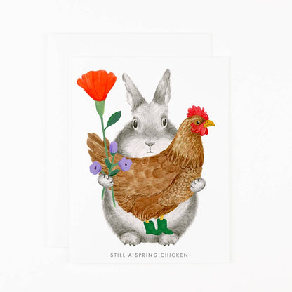 Illustrated greeting card with grey bunny hugging a brown chicken, orange flower, purple blossoms