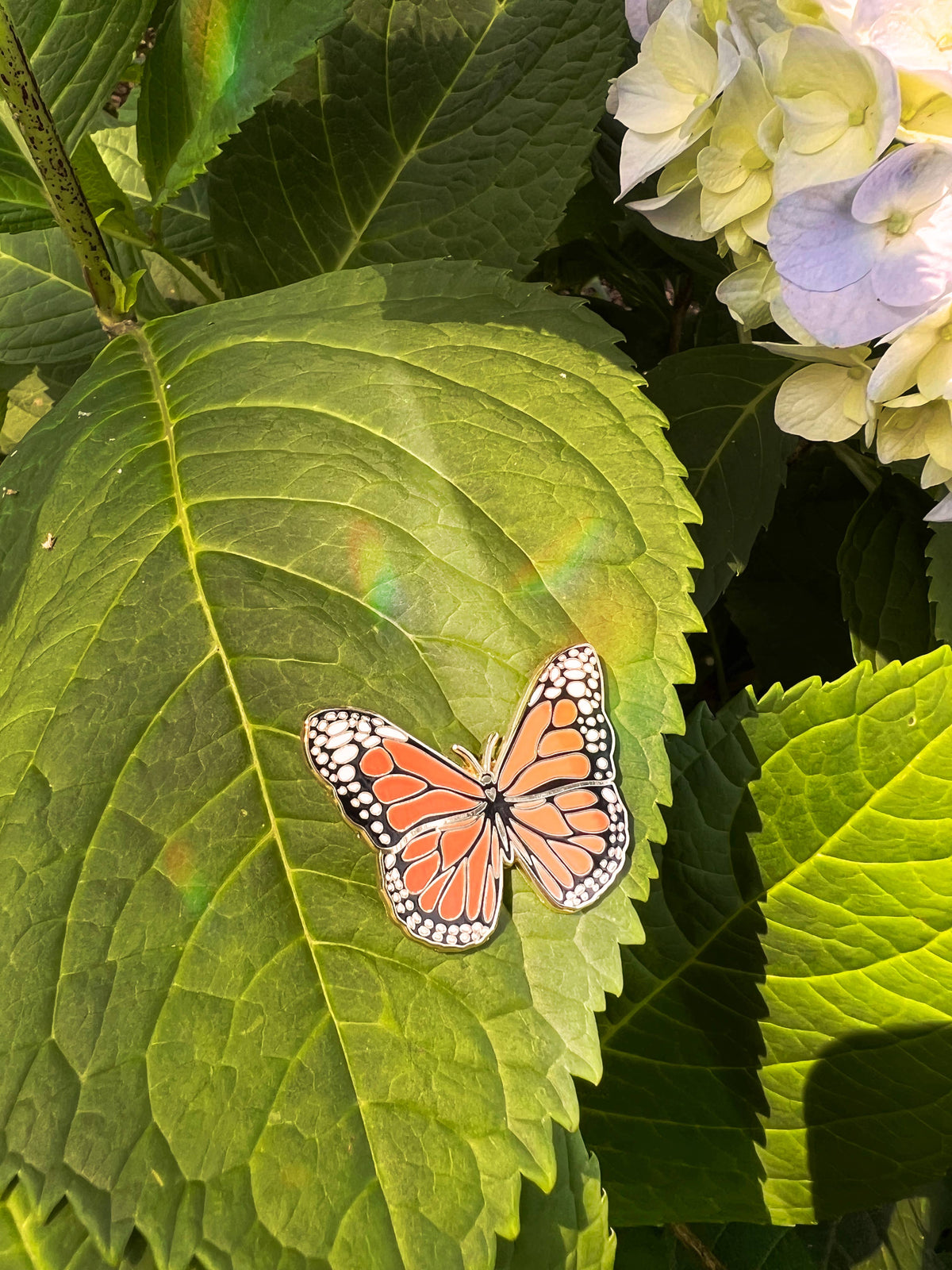 Monarch butterfly pin on a large green leaf, black-and-orange enamel details.
