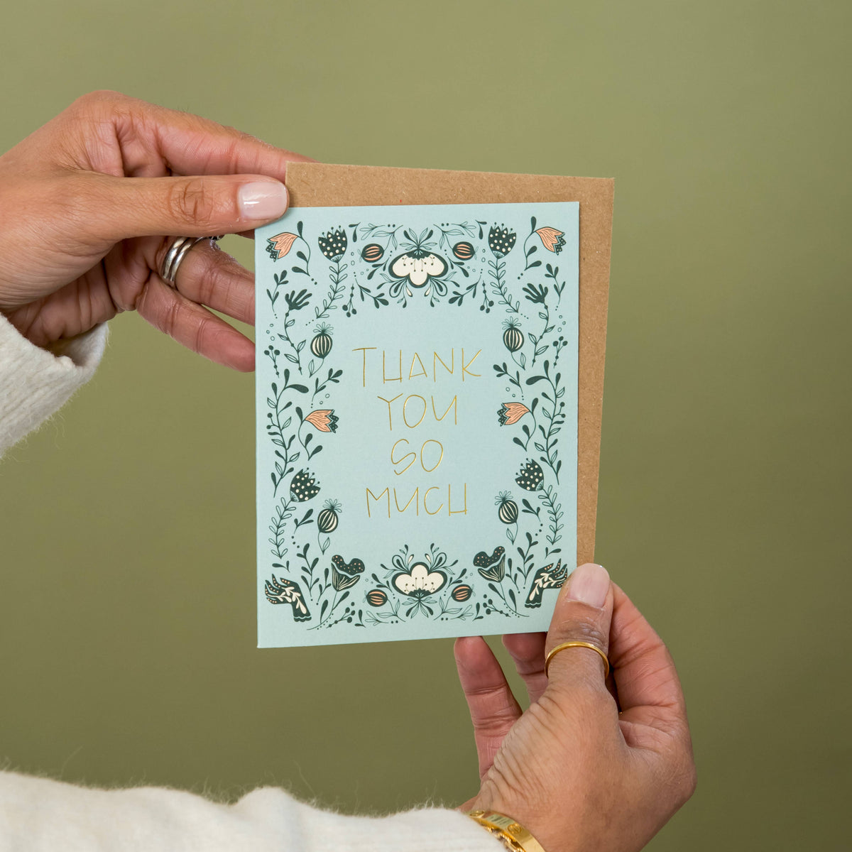 Thank you greeting card with gold foil lettering, floral border and kraft envelope held in hands