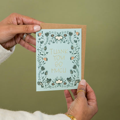 Thank you greeting card with gold foil lettering, floral border and kraft envelope held in hands