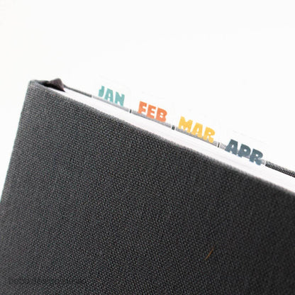 Planner month index sticker tabs on clear strip edge: JAN, FEB, MAR, APR