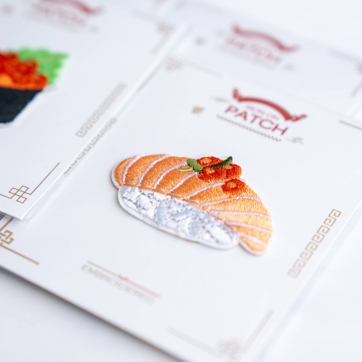 Close-up salmon nigiri embroidered iron-on patch on card with green garnish
