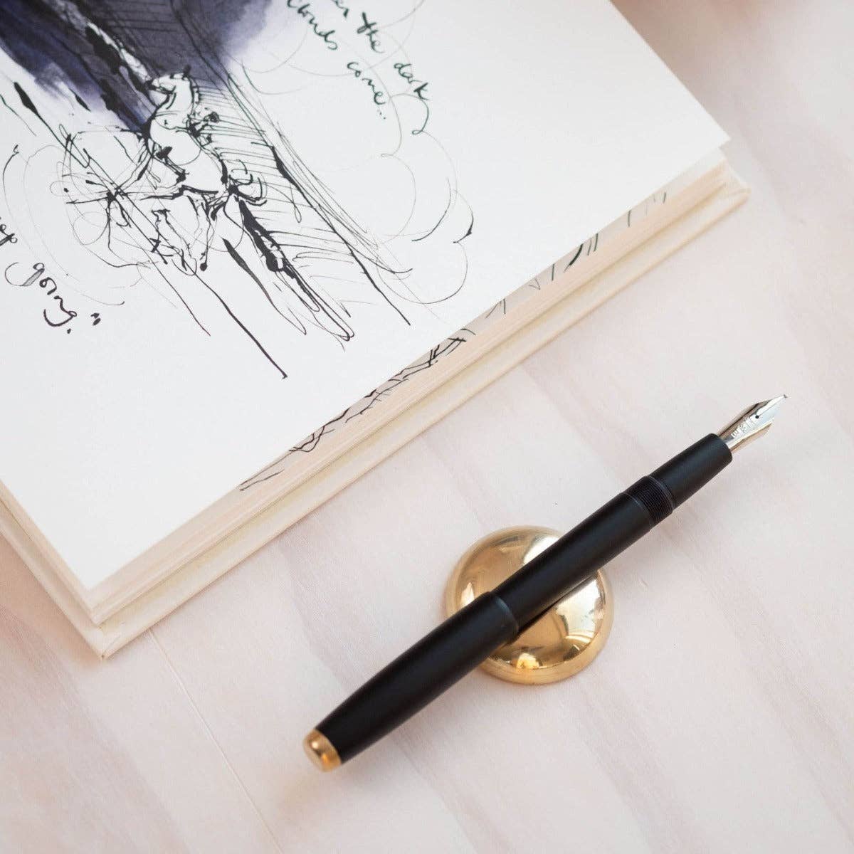 Black fountain pen with gold nib and cap end, beside a notebook sketch.