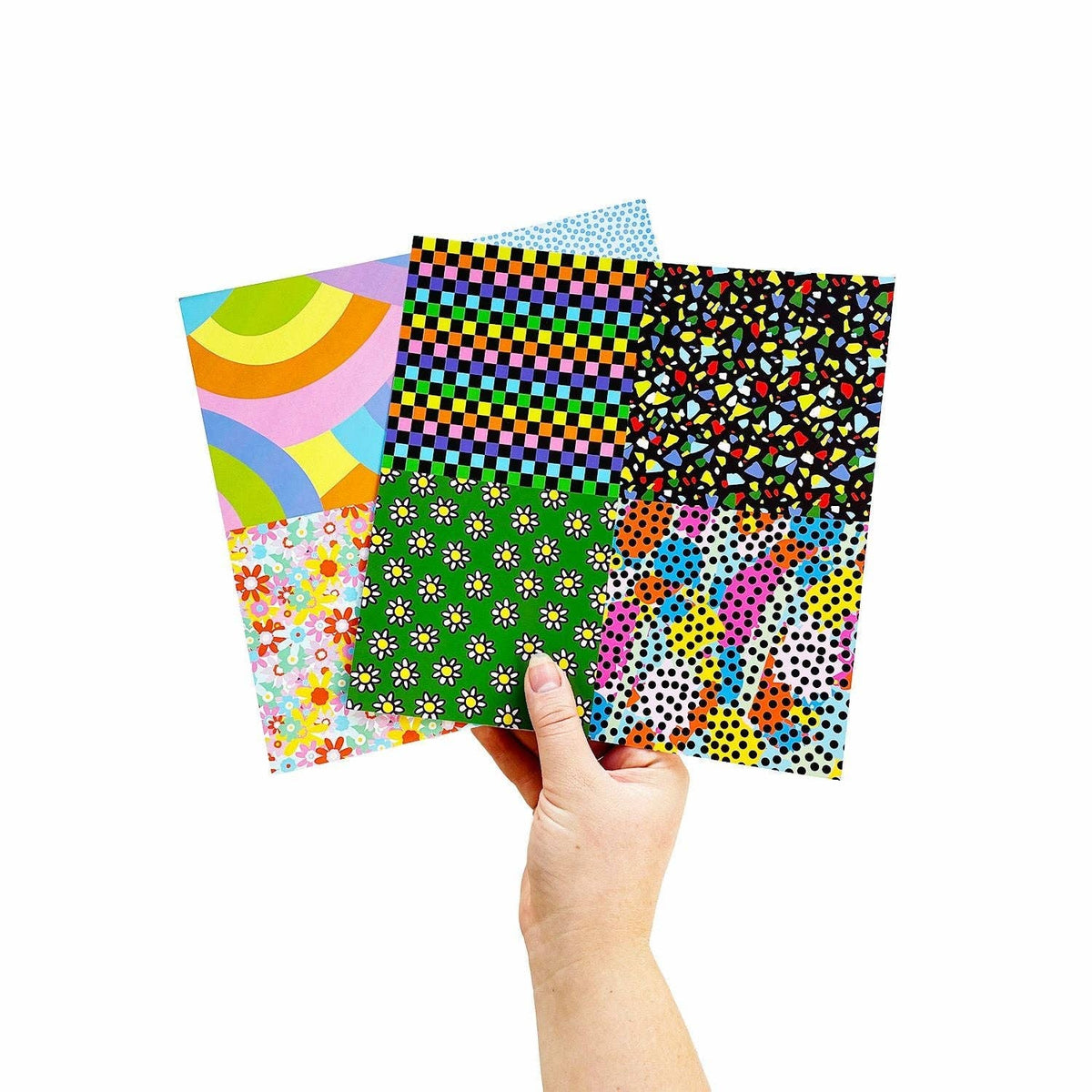 Hand holding four patterned sticker sheets: geometric, floral, and confetti