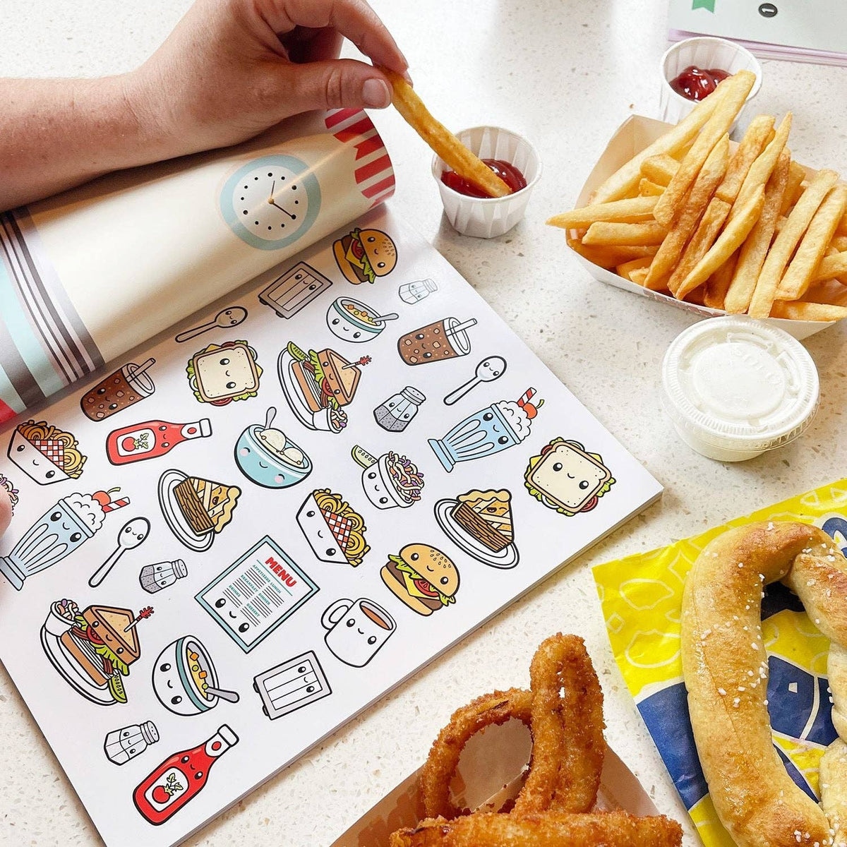 Food sticker book open with cartoon meal and drink stickers beside fries and sauce
