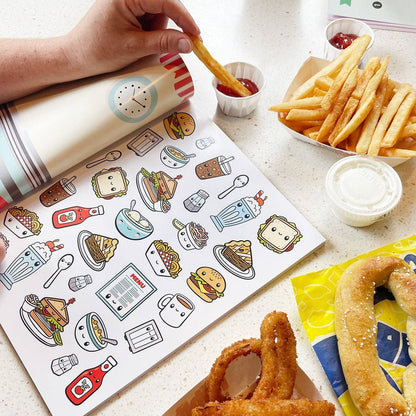 Food sticker book open with cartoon meal and drink stickers beside fries and sauce