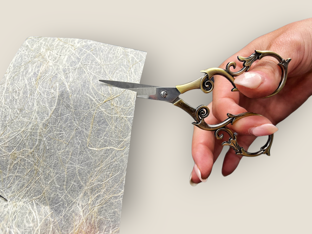 Ornate scissors held in hand, cutting through textured paper
