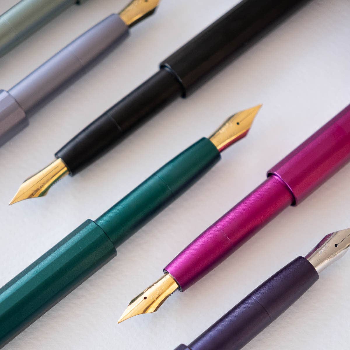 Pocket fountain pens in green, magenta, purple, and black with gold nibs.