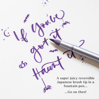Silver brush-tip pen applying purple ink calligraphy strokes on paper