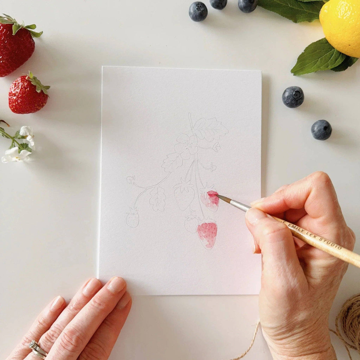 Paintable notecard with pencil fruit outlines; hand painting with watercolor brush.