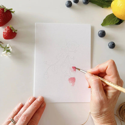 Paintable notecard with pencil fruit outlines; hand painting with watercolor brush.