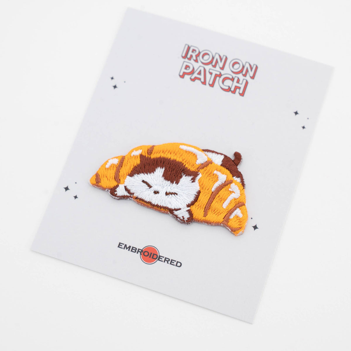 Iron-on cat food patch: curled cat sleeping on orange croissant slice, embroidered detail