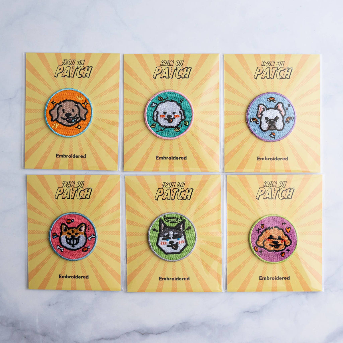 Six round embroidered dog iron-on patches in a grid on yellow cards