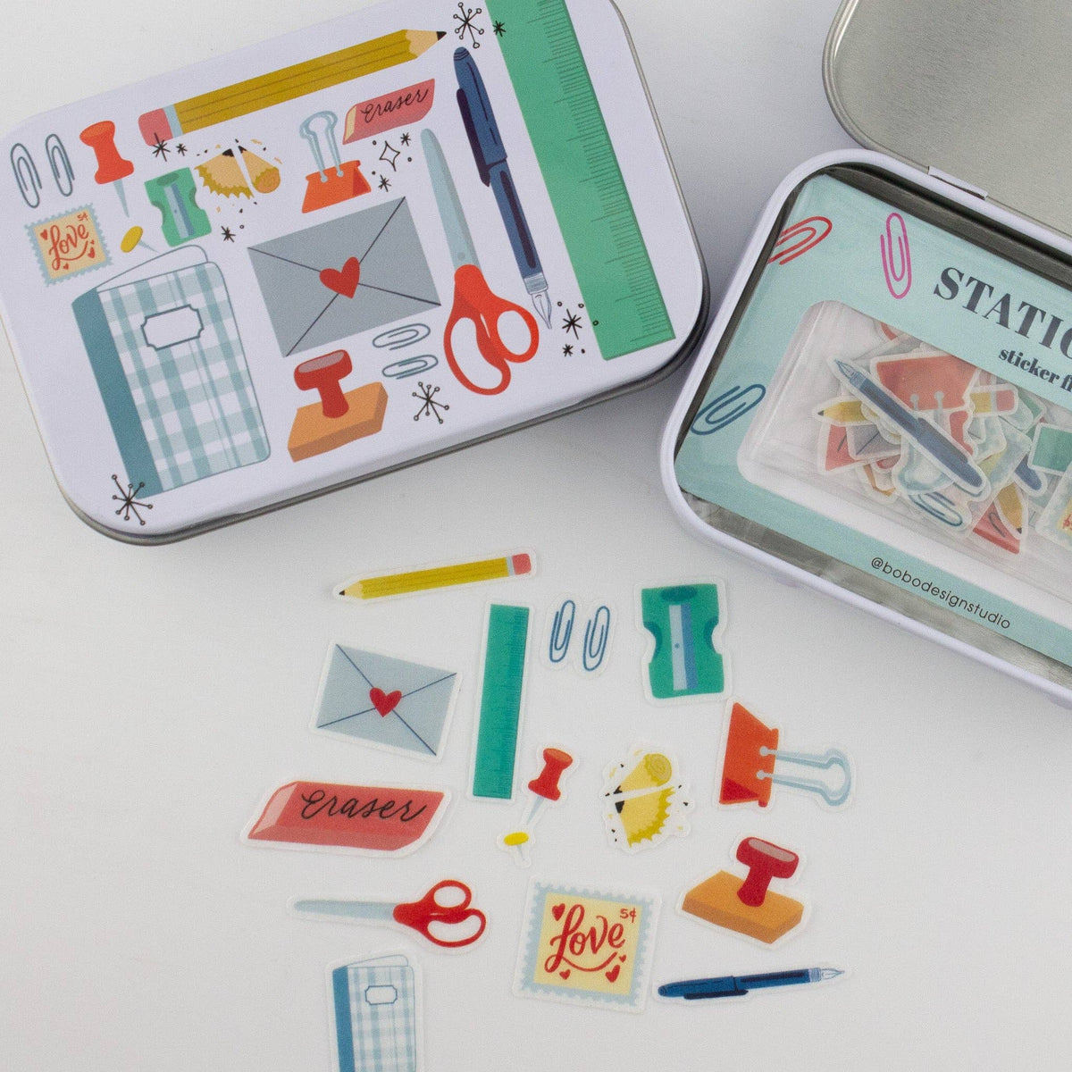 Close-up stationery trinket tins with illustrated fronts and sticker flakes on surface
