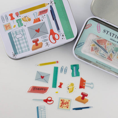Close-up stationery trinket tins with illustrated fronts and sticker flakes on surface