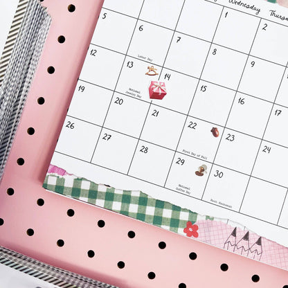 Close-up of wall calendar date grid with small icons and decorative ribbon border at the bottom.