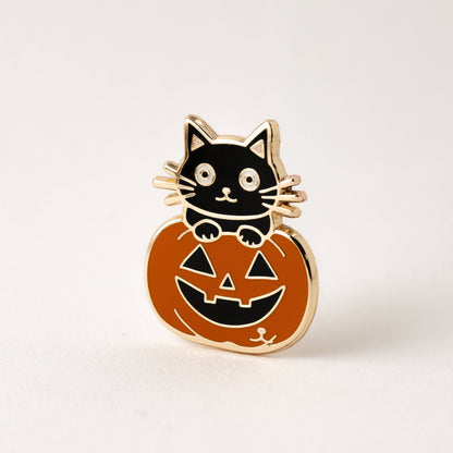 Enamel Halloween cat pin on orange jack-o’-lantern with black outline and gold backing