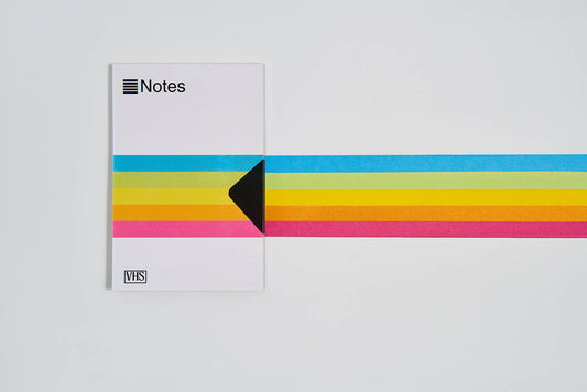 VHS notes notepad with rainbow stripe band, black corner arrow, and VHS label