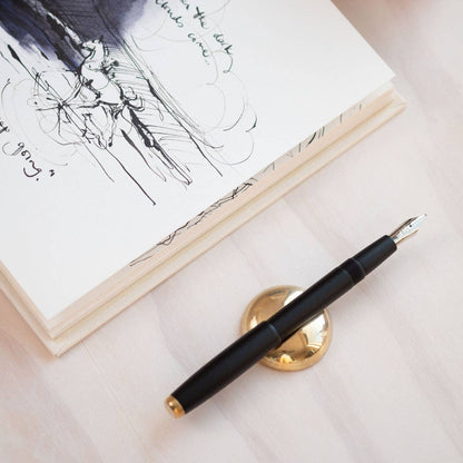 Solid brass pen rest with black fountain pen resting on the base