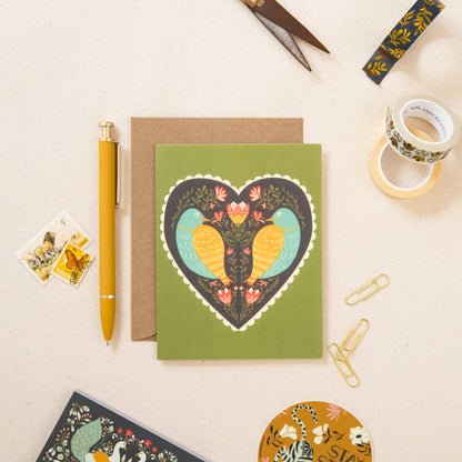 Green greeting card featuring two colorful birds in a heart-shaped floral design