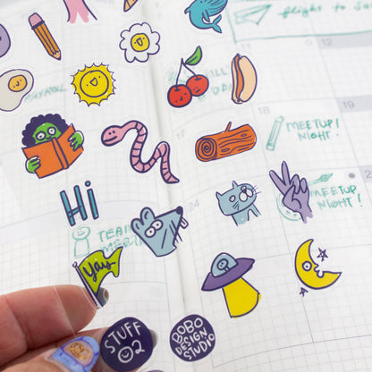 Clear sticker sheet in hand with applied stickers, including “STUFF 02” and “MEETUP NIGHT”