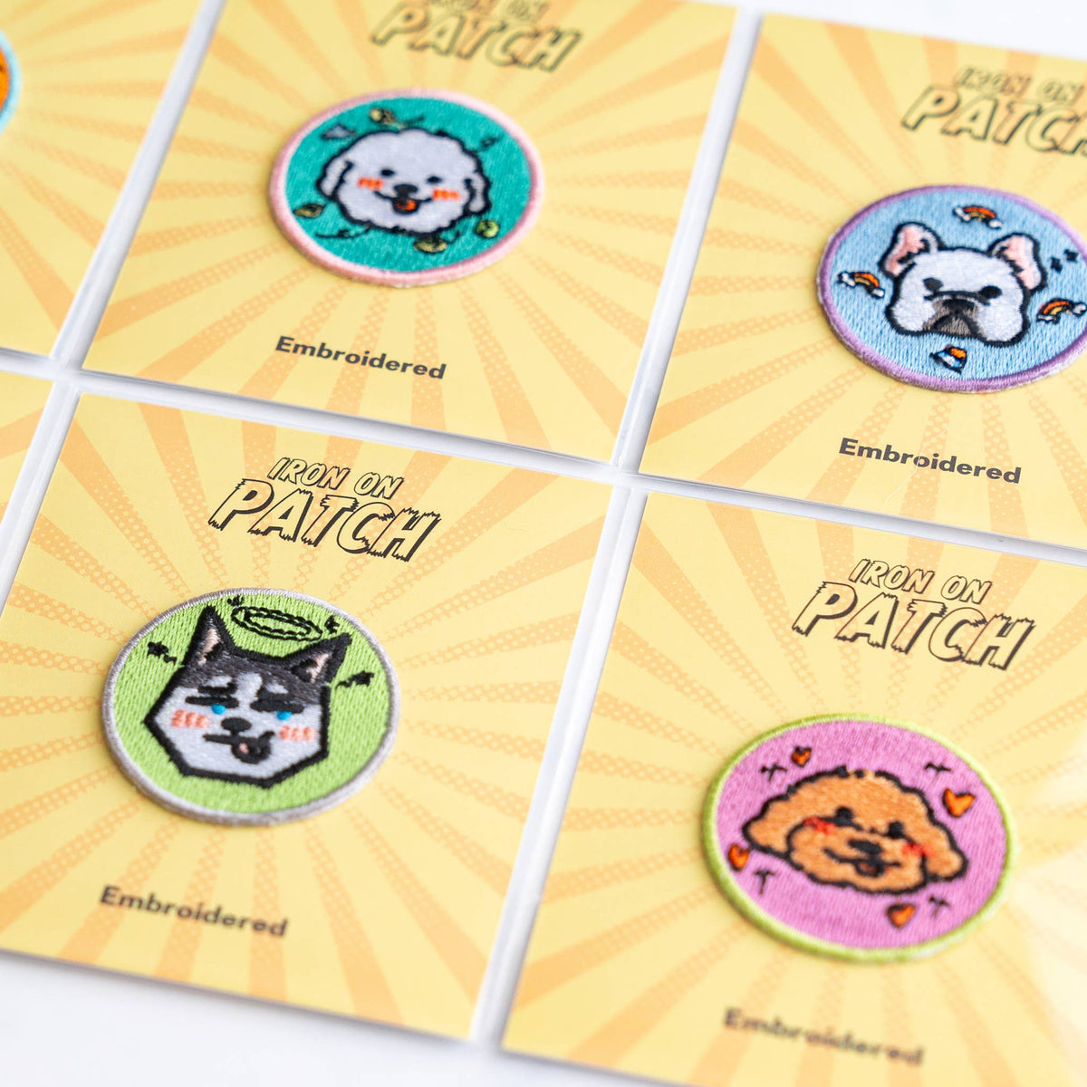 Close-up of four round embroidered dog iron-on patches on yellow cards
