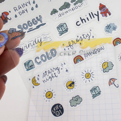 Hand holding weather sticker sheet with rainy day, soggy, windy, cold, and rainbow icons