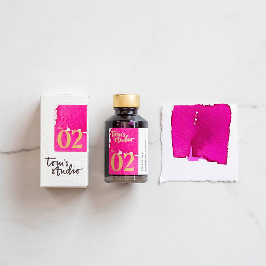 Fountain pen ink bottle with gold cap and raspberry-pink ink swatch cards