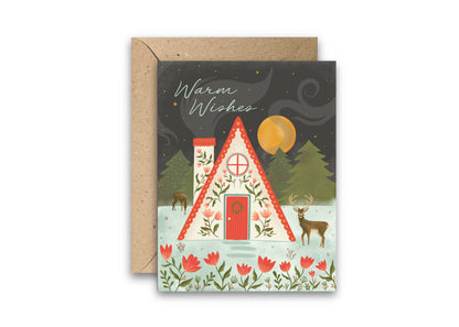 Woodland Christmas greeting card with a decorated cabin, deer, trees, and matching kraft envelope
