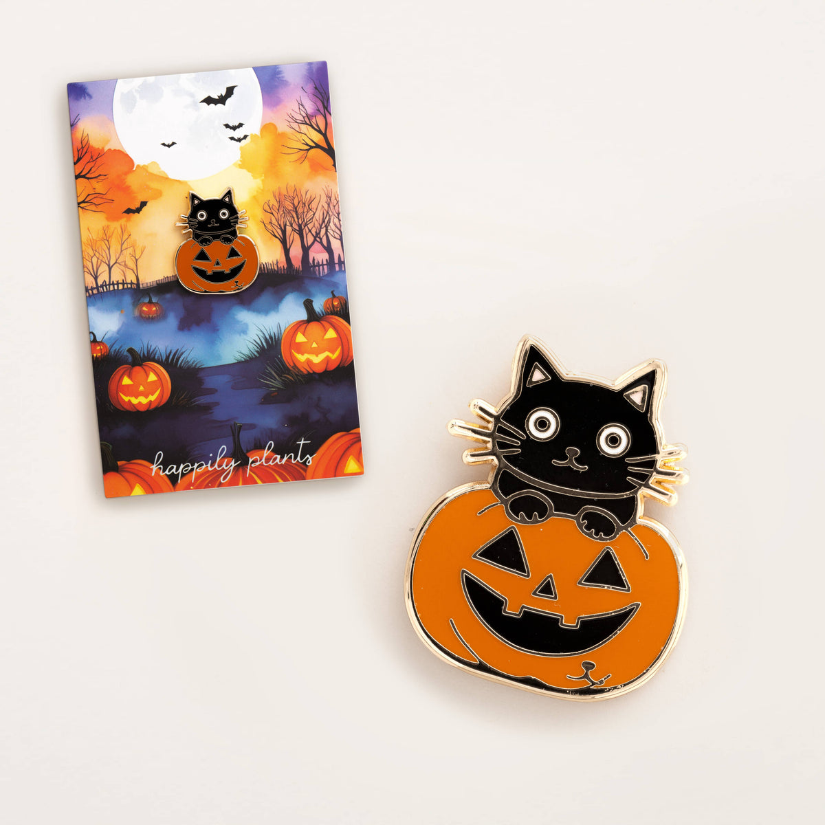 Halloween cat pumpkin enamel pin next to illustrated greeting card