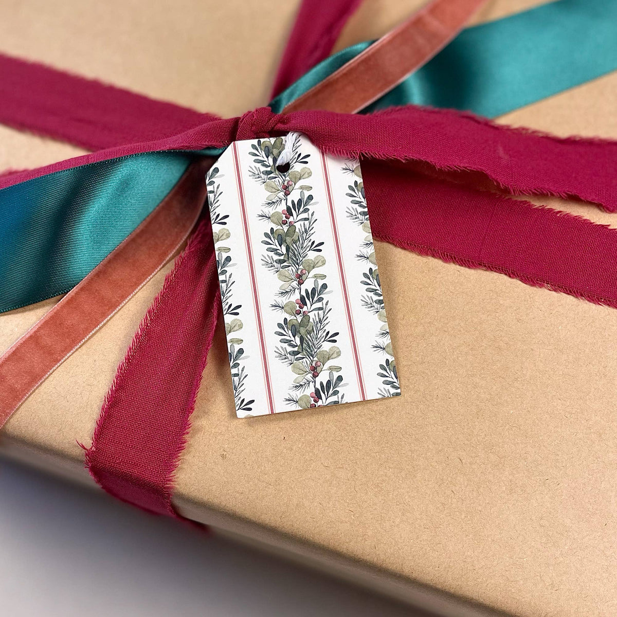 Christmas gift tag with greenery and berries pattern, tied to a maroon and teal ribbon