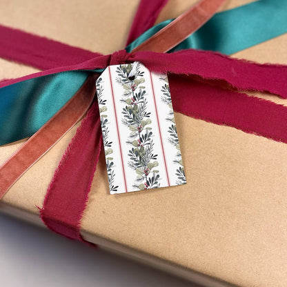Christmas gift tag with greenery and berries pattern, tied to a maroon and teal ribbon
