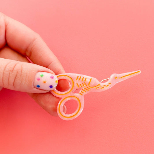Pink scissors-shaped hair clip with orange ring tips and decorative lines