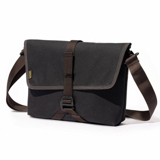 Dark canvas crossbody sling bag with front flap, adjustable strap, and side snap buckle