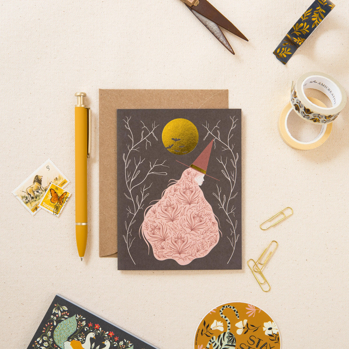 Witch greeting card with gold moon and kraft envelope, shown with stationery accessories