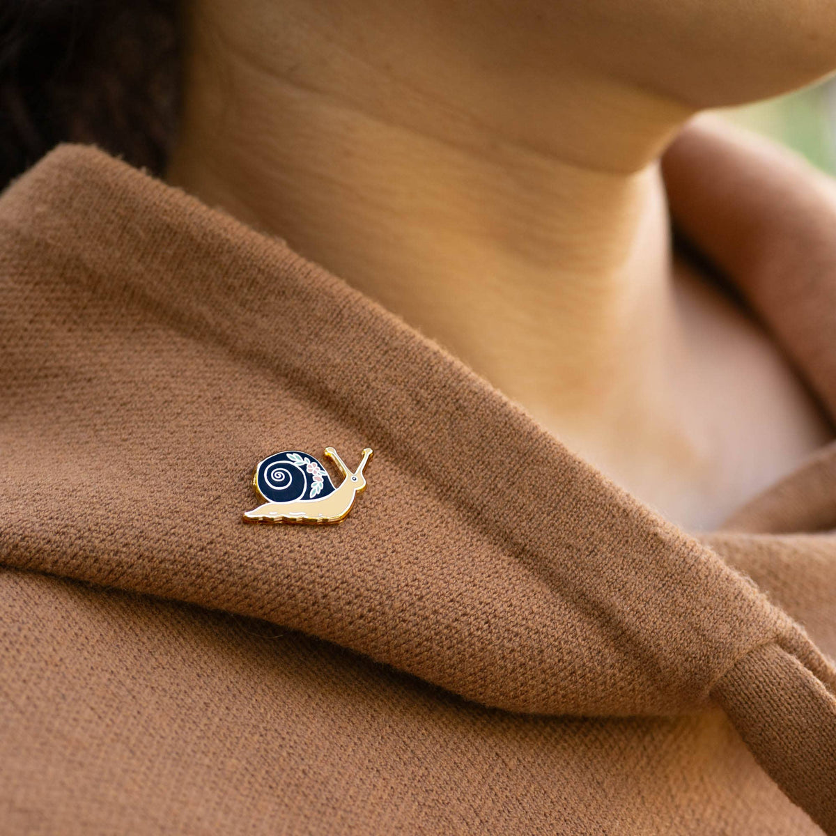 Enamel garden snail lapel pin on brown fabric, black swirl shell with flower detail