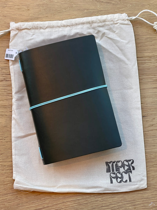 B6 notebook with dark cover and teal elastic band, in a white drawstring pouch