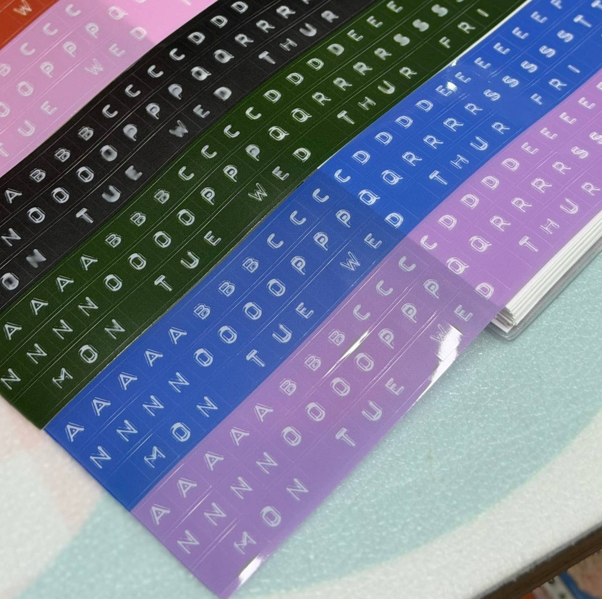 Embossed letters kiss-cut PET tape sheets on clear backing with blue, green and lavender letters