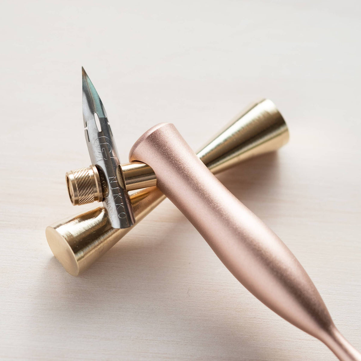 Brass pen rest holding two pens: rose-gold and black, in conical holders