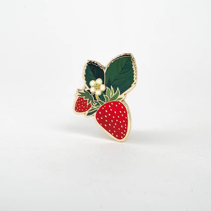Strawberry blossom enamel pin with red berries, white dots, green leaves, and white flower