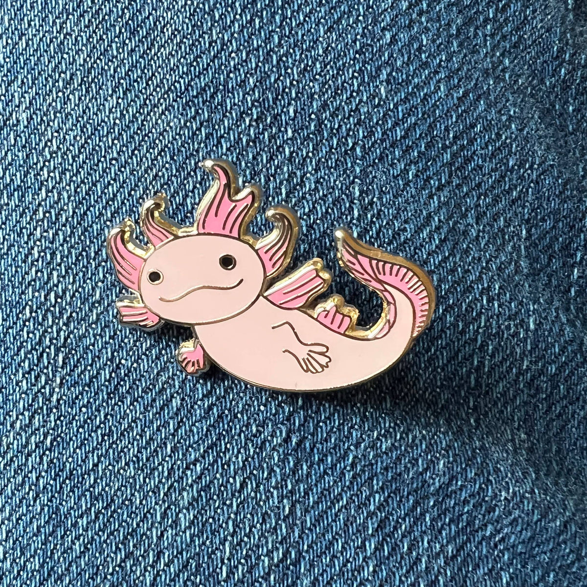 Close-up pink axolotl enamel lapel pin with gold border on denim