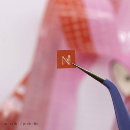 Orange embossed letter tape square with silver blade tool cutting a letter