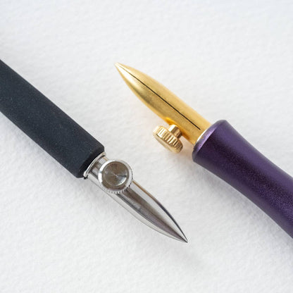 Close-up of two dip pen nibs: silver on black and gold on purple handles