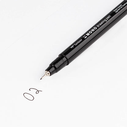 Black fine-tip drawing pen writing a small “0.2” sketch on white paper