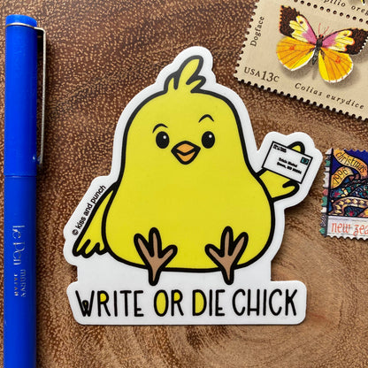 Yellow chick sticker with “Write or Die Chick” lettering, shown beside a pen for scale