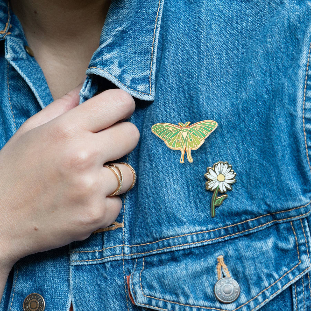 Luna moth enamel pin on blue denim jacket pocket, green wings with gold outline