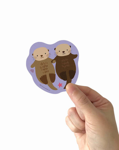 Sea otters vinyl sticker held by a finger, showing two sea otters and pink star